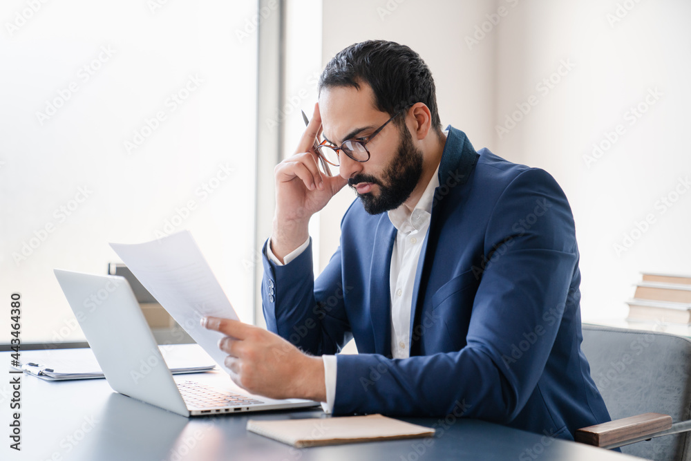 Concentrated tired stressed depressed serious arabian businessman having problems at workplace, solving job issues, doing paperwork. Deadline, paying bills, debt and loan concept. Headache migraine Concentrated tired stressed depressed serious arabian businessman having problems at workplace, solving job issues, doing paperwork. Deadline, paying bills, debt and loan concept. Headache migraine
