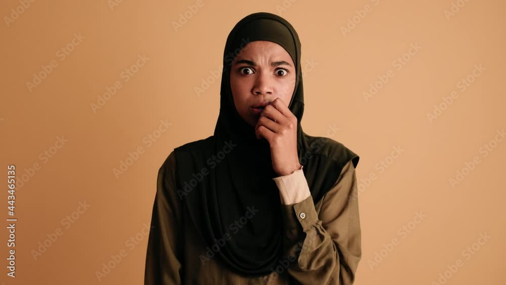 A shocked sacred arabian woman is looking to the camera standing isolated over beige background A shocked sacred arabian woman is looking to the camera standing isolated over beige background