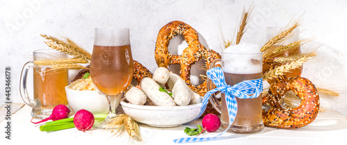Oktoberfest food background, Traditional bavarian holiday food menu, sausages with pretzels, sauerkraut, beer glass and mugs on white wooden sun lighted background wide banner