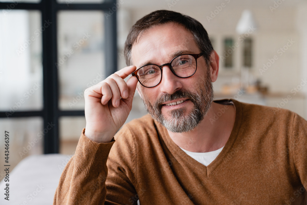 Obraz premium Portrait of a confident Caucasian mature middle-aged man wearing glasses sitting at home on quarantine. Father husband relaxing on sofa on social distance.