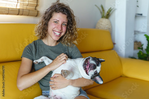 Woman dog lover with bulldog at home on the couch. Horizontal view of woman tickling her dog.