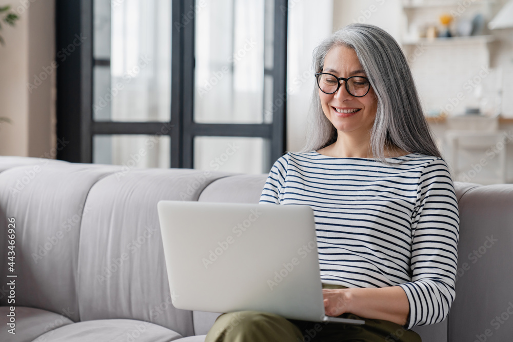 Naklejka premium Busy middle-aged mature businesswoman tutor mother wife using laptop for e-learning, searching web, online shopping, remote freelance work, watching movies.