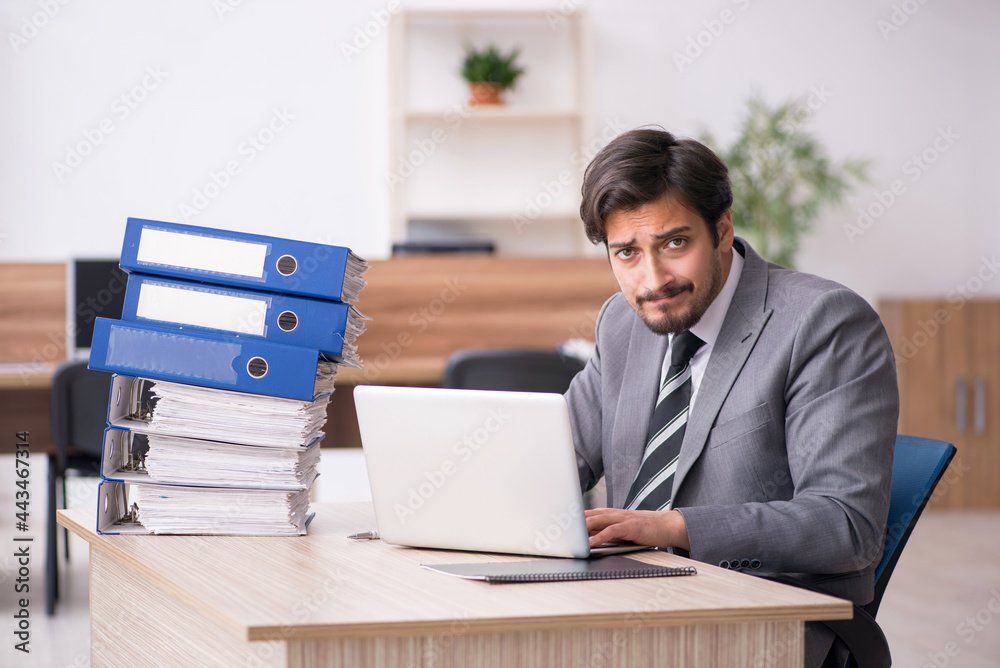 Young male employee unhappy with excessive work in the office Young male employee unhappy with excessive work in the office