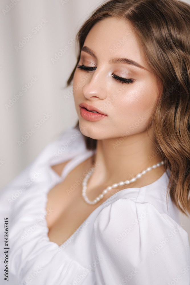 Portrait of young and elegant female in white dress with beautiful makeup and hairstyle. Gorgeous model posing to photographer in studio