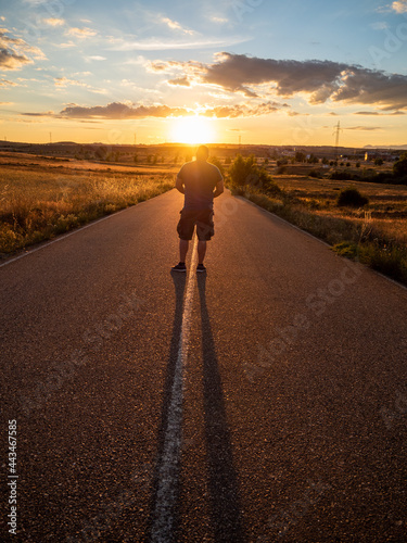 Strong man with his back turned on a road with the sun facing him at sunset. Summer sport image