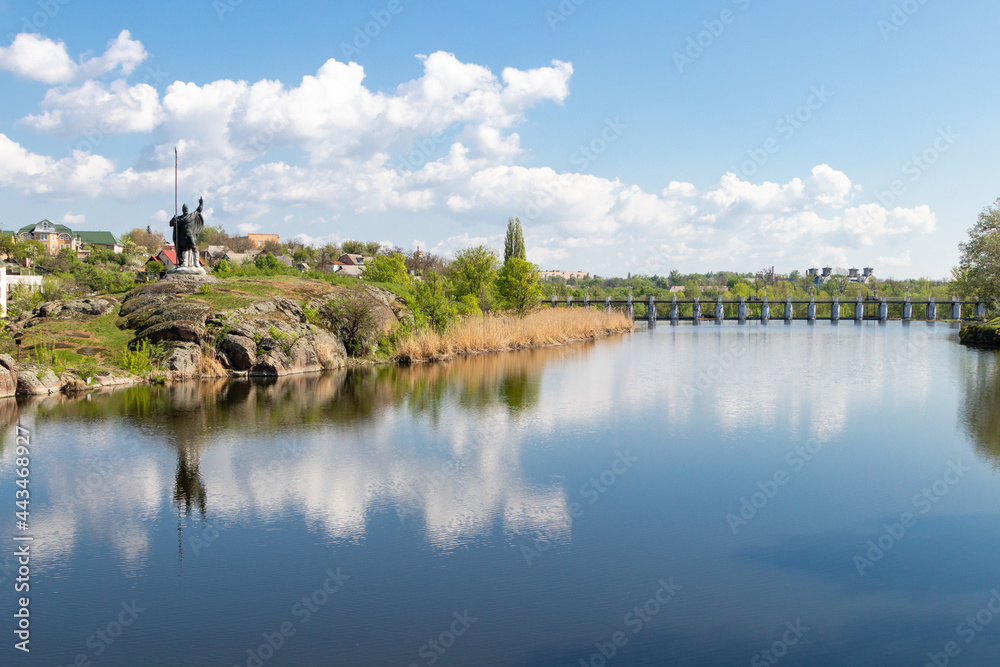Fototapeta premium green coast of a beautiful small river with white clouds in reflection