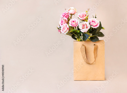 Bouquet of pink roses in craft paper bag on brown background