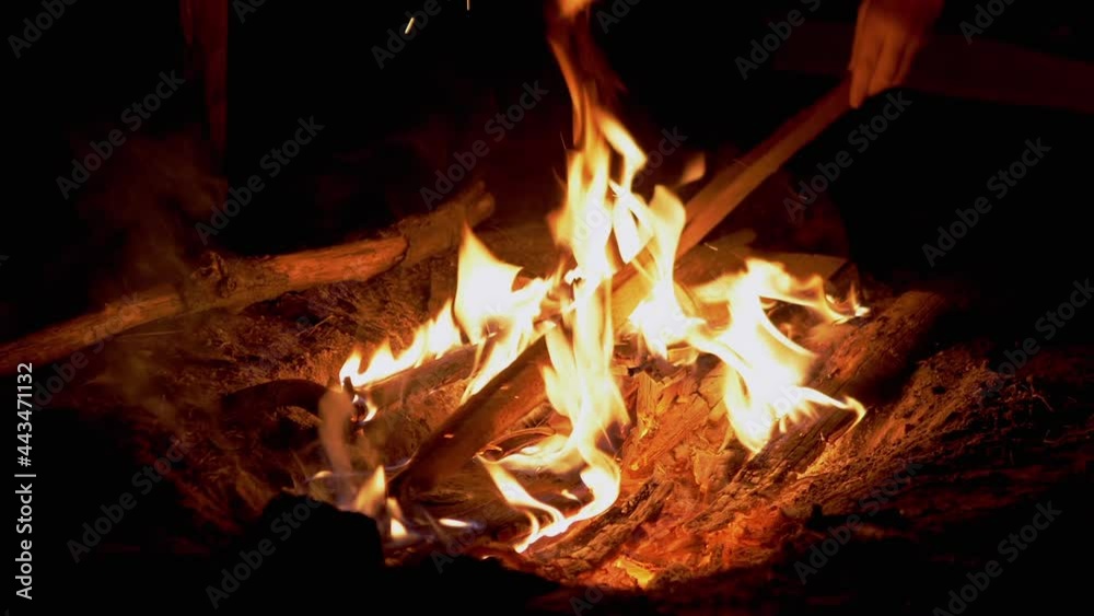 Male in Forest Throws Sticks, Branches, Firewood in a Burning, Night Bonfire. Dry Firewood, log, branches burn and smolder in open fire in a pit with smoke. Camping. Tourism summer. Zoom. Slow motion. Male in Forest Throws Sticks, Branches, Firewood in a Burning, Night Bonfire. Dry Firewood, log, branches burn and smolder in open fire in a pit with smoke. Camping. Tourism summer. Zoom. Slow motion.