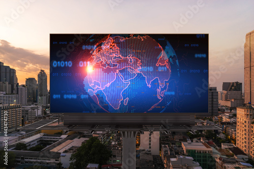 Glowing hologram of Earth planet map on billboard over aerial panoramic cityscape of Bangkok at sunset. The concept of international business in Southeast Asia.