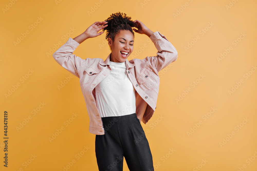 Inspired black girl in jacket posing with hands up. Studio shot of relaxed african american woman isolated on yellow background. Inspired black girl in jacket posing with hands up. Studio shot of relaxed african american woman isolated on yellow background.