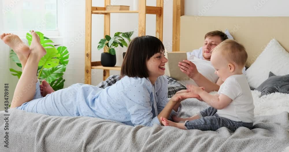 Mother playing with baby son while father reading book on bed at home Mother playing with baby son while father reading book on bed at home