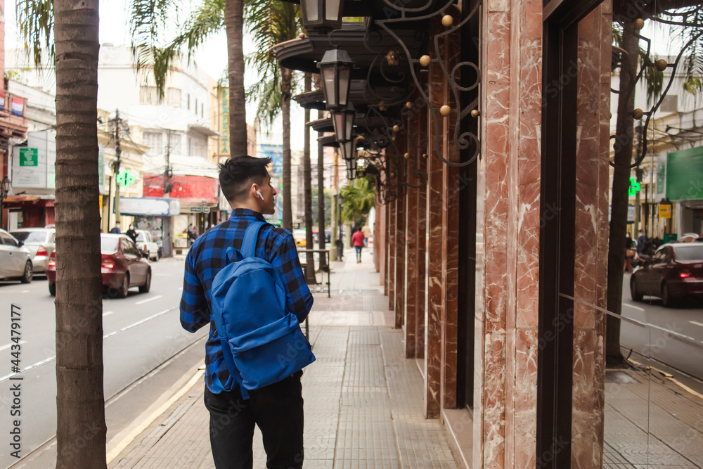 Rear view of a man with a backpack and wireless headphones walking the streets of the city. Rear view of a man with a backpack and wireless headphones walking the streets of the city.
