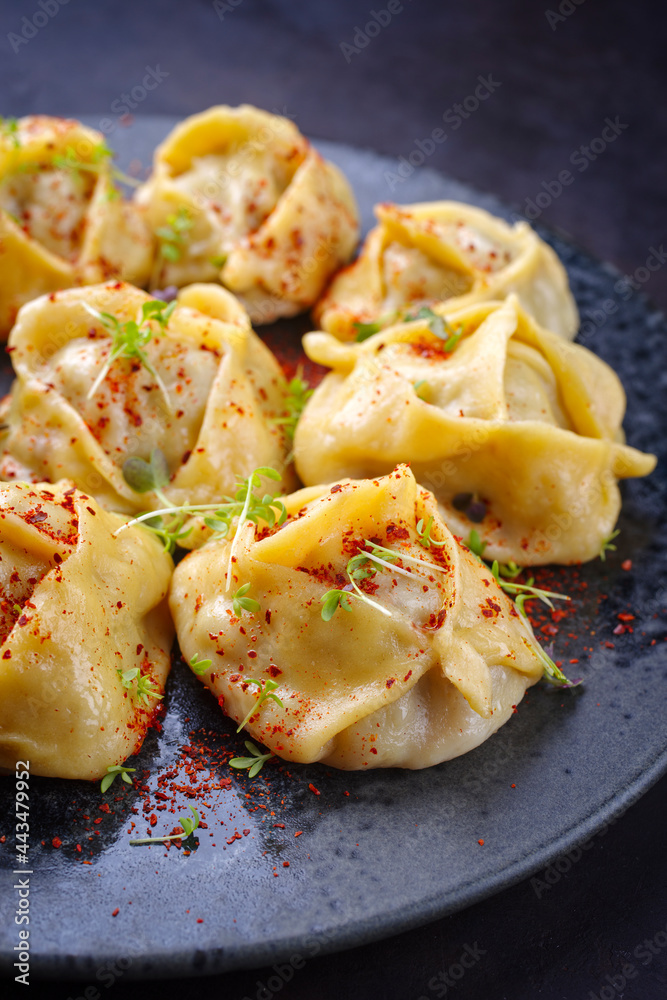 Traditional steamed Kazakh manti garnished with mincemeat and sumah served as close-up on a Nordic design plate
