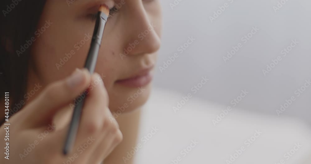 Young middle eastern woman applying shadows on eyes, making make-up herself, tracking shot from palette on face