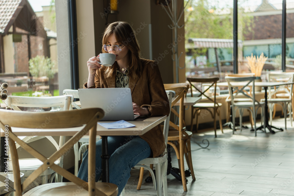 Trendy freelancer drinking coffee while using laptop in cafe. Trendy freelancer drinking coffee while using laptop in cafe.