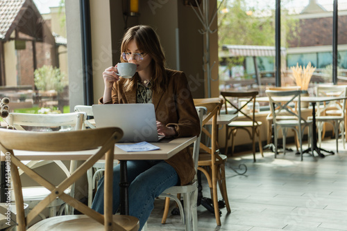 Trendy freelancer drinking coffee while using laptop in cafe. © LIGHTFIELD STUDIOS