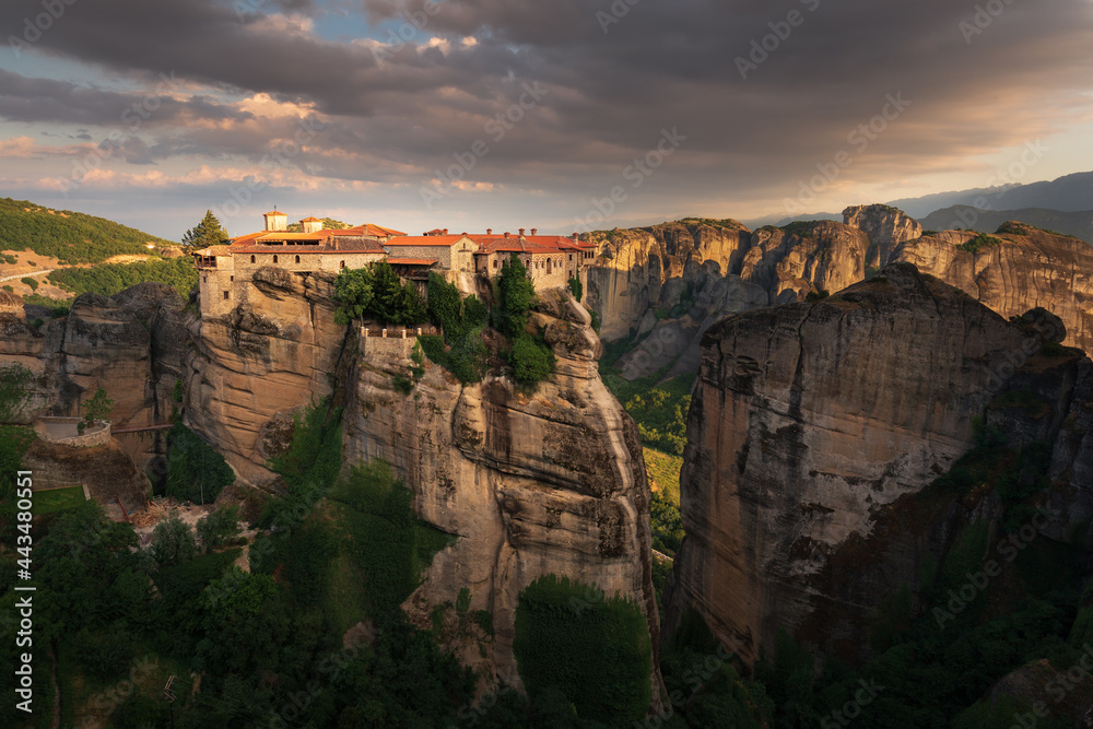 Scenic sunset landscape of a mountain valley in Greece with bizarre cliffs, a dense forest at the foot of the mountains, and an old Christian monastery on top of a cliff