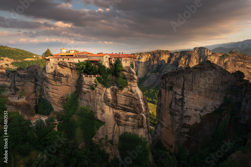 Scenic sunset landscape of a mountain valley in Greece with bizarre cliffs, a dense forest at the foot of the mountains, and an old Christian monastery on top of a cliff