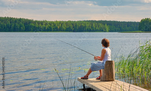 woman fishing on spinning rod at forest lake on summer evening, angler