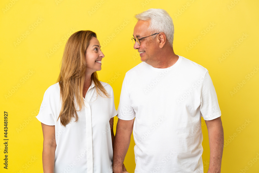Middle age couple isolated on yellow background looking at each other Middle age couple isolated on yellow background looking at each other
