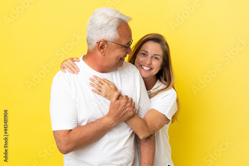 Middle age couple isolated on yellow background laughing and hugging