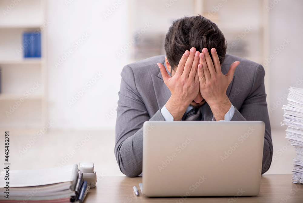 Young male employee unhappy with excessive work in the office Young male employee unhappy with excessive work in the office
