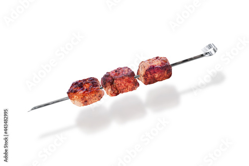 Cooked shish kebab, three pieces of juicy meat on skewer, isolated on white background.