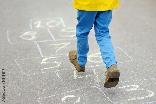 Little boy's legs and hopscotch drawn on asphalt. Child playing hopscotch game on playground on spring day.