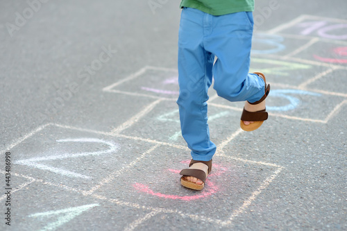 Little boy s legs and hopscotch drawn on asphalt. Child playing hopscotch game on playground on spring day.