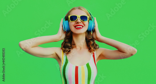 Portrait of happy laughing young woman listening to music in headphones on green background