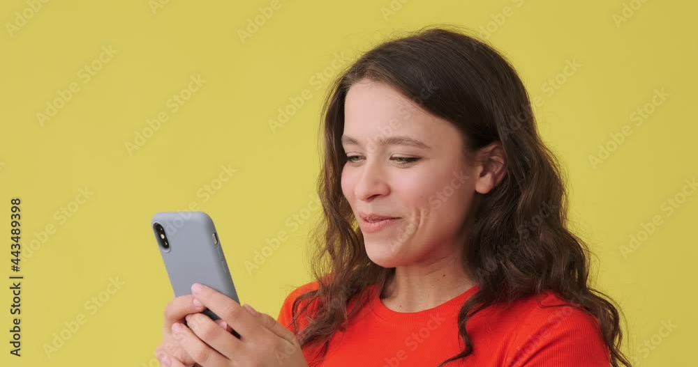 Happy woman text messaging on mobile phone over yellow background Happy woman text messaging on mobile phone over yellow background