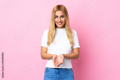 Young Uruguayan blonde woman over isolated pink background holding copyspace imaginary on the palm to insert an ad