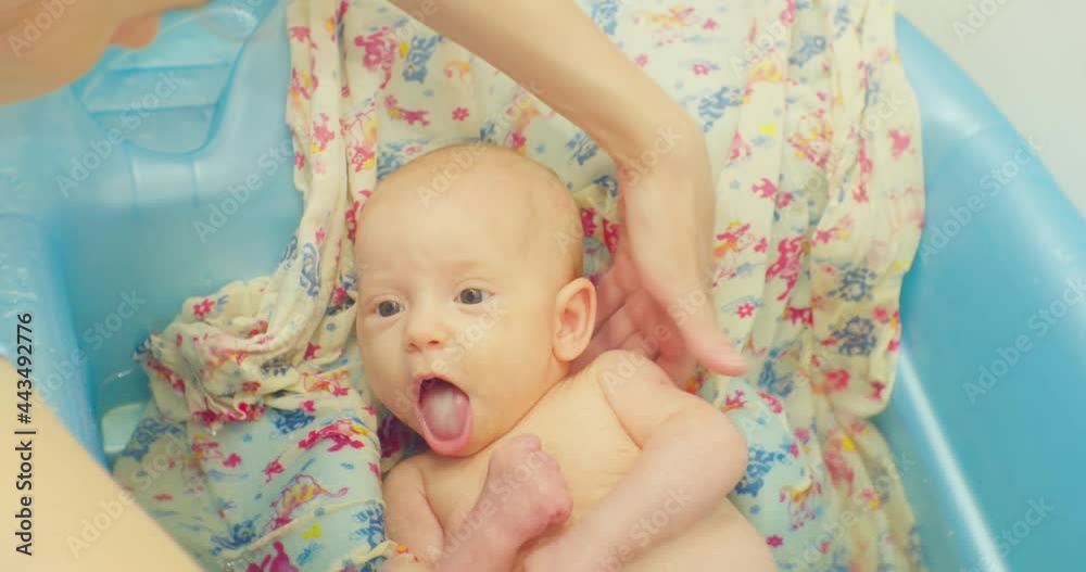 caring female hands wash a little cute baby lying on a bright sheet in a baby bath. caring female hands wash a little cute baby lying on a bright sheet in a baby bath.