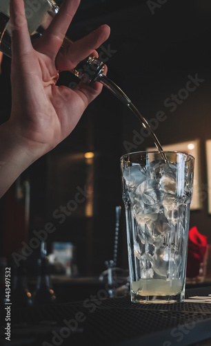 bartender hand mixing cocktail Lemonade with ice cubes in glass to customers at bar 