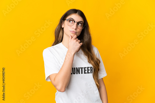 Young volunteer woman isolated on yellow background having doubts