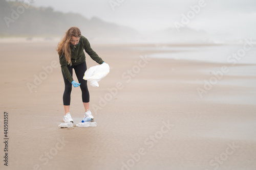 A young blonde woman, a volunteer, cleans up the debris on the ocean shore, which was taken out by the waves. Involvement in the problem of environmental pollution.