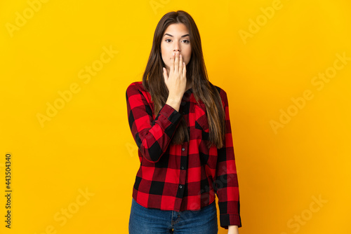 Teenager Brazilian girl isolated on yellow background covering mouth with hand