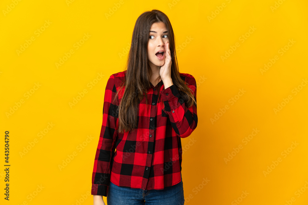 Teenager Brazilian girl isolated on yellow background whispering something with surprise gesture while looking to the side Teenager Brazilian girl isolated on yellow background whispering something with surprise gesture while looking to the side