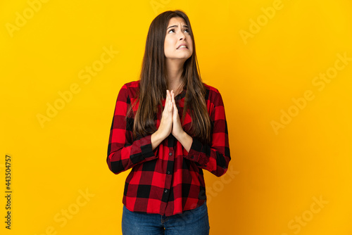 Teenager Brazilian girl isolated on yellow background keeps palm together. Person asks for something © luismolinero