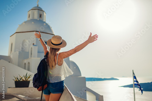 Woman tourist raised arms looking at Caldera sea landscape in Fira, Santorini island walking by traditional church. photo