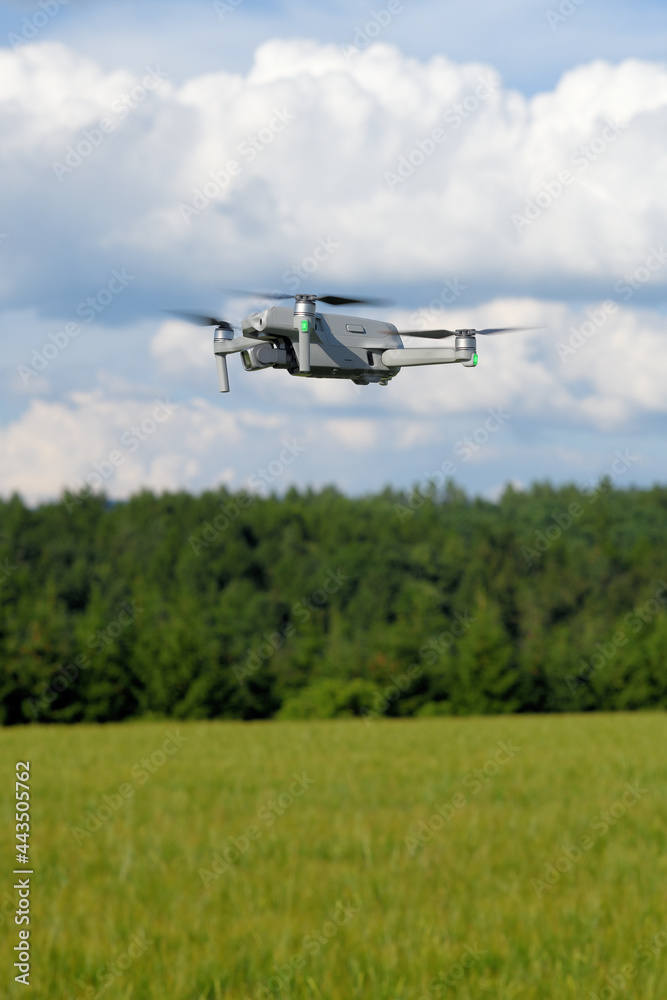 Side view of a flying modern UAV drone on yellow corn field a blue sky background. UAV drone copter flying with high resolution digital camera on the blue sky. Side view of a flying modern UAV drone on yellow corn field a blue sky background. UAV drone copter flying with high resolution digital camera on the blue sky.