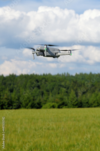 Side view of a flying modern UAV drone on yellow corn field a blue sky background. UAV drone copter flying with high resolution digital camera on the blue sky.