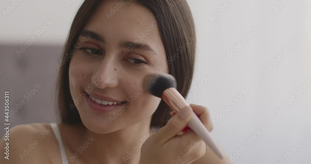 Young attractive middle-eastern lady applying rouge on her face with make-up brush, finishing everyday makeup at home Young attractive middle-eastern lady applying rouge on her face with make-up brush, finishing everyday makeup at home