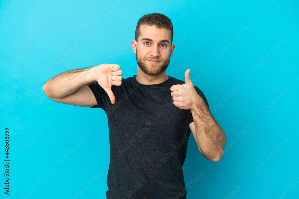 Young handsome caucasian man isolated on blue background making good-bad sign. Undecided between yes or not Young handsome caucasian man isolated on blue background making good-bad sign. Undecided between yes or not