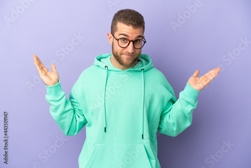 Young handsome caucasian man isolated on purple background making doubts gesture © luismolinero