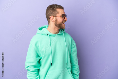 Young handsome caucasian man isolated on purple background laughing in lateral position