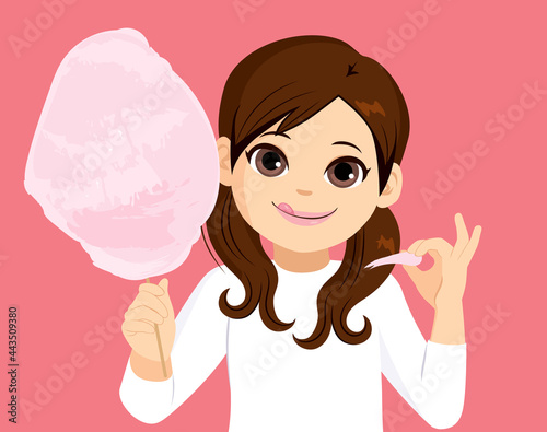 Cute little girl eating delicious tasty cotton candy floss picking on pink background