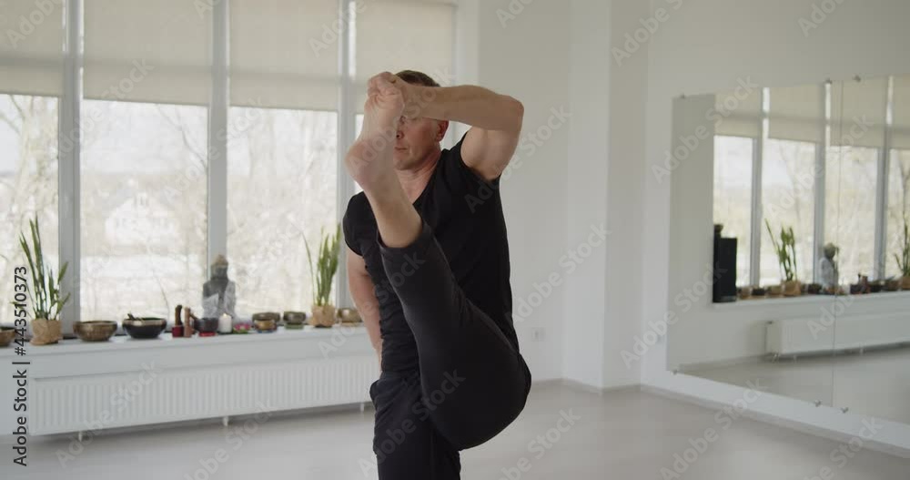 Professional trainer practices flow yoga in private class. Adult man makes yoga asanas on a mat in white bright studio. Fitness, healthy lifestyle and wellness concept.