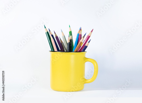 colored pencils in a yellow coffee mug on white background