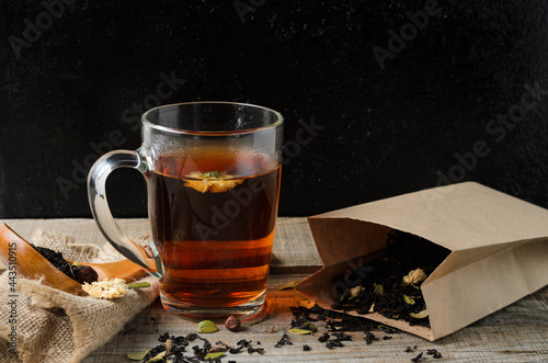 A glass mug of fragrant brewed flower tea on a wooden table, with tea leaves in a paper package, in a rustic style.